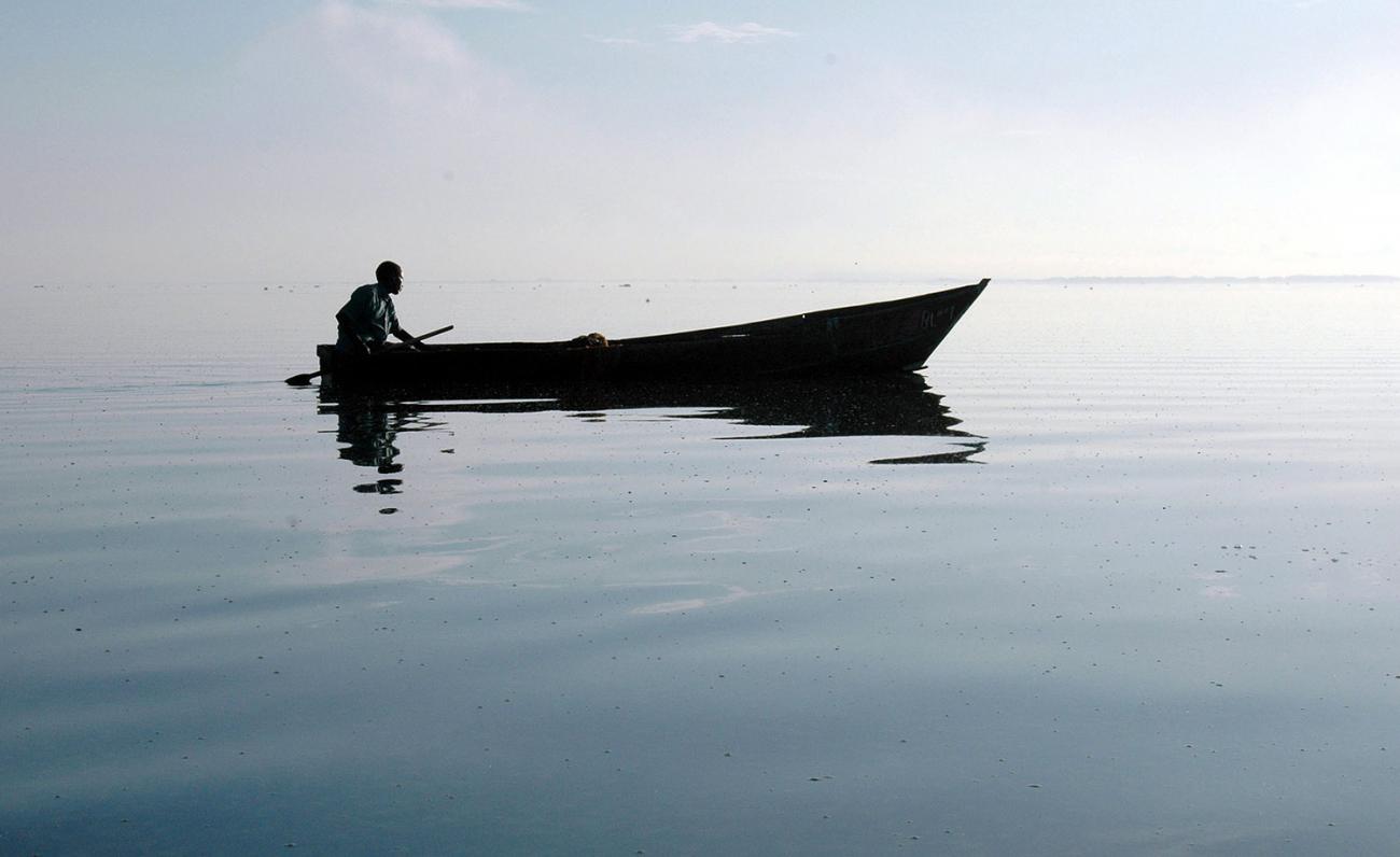A Ugandan fisherman rows back to his nets at dawn on Uganda's Lake Victoria on March 21,2006. The picture shows the man on a long boat, silhouetted against a placid lake surface. The weather is calm. He is wearing no life vest.