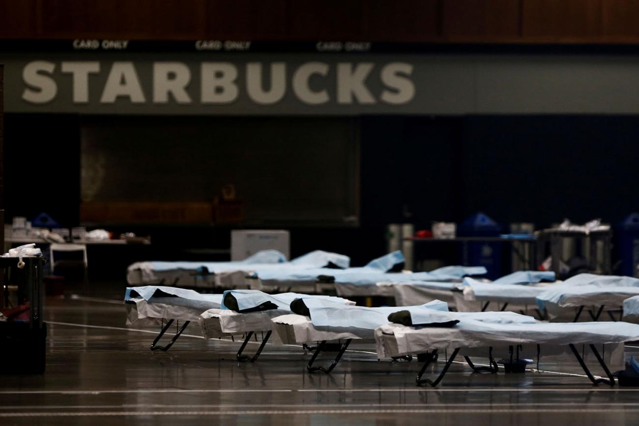 The photo shows a large number of beds lined up in a large open space with a Starbucks sign in the background. 