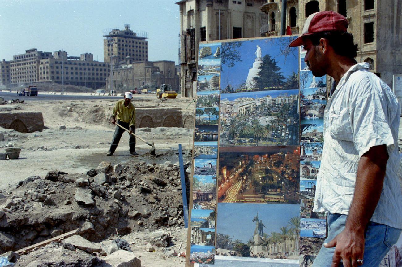 The image shows a poster vendor standing next to a field of rubble.