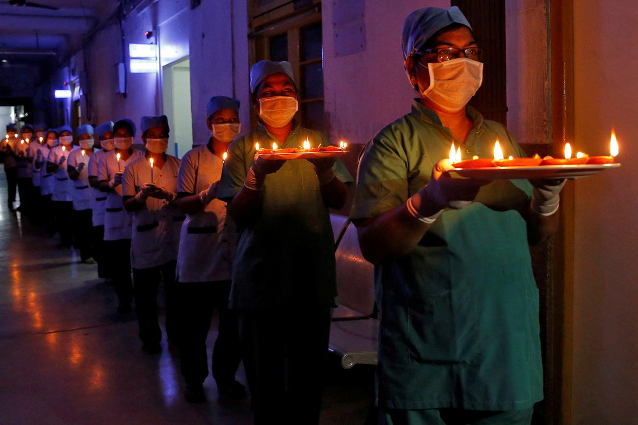 The photo shows a long procession of health care workers carrying candles down a dimply lit corridor. 