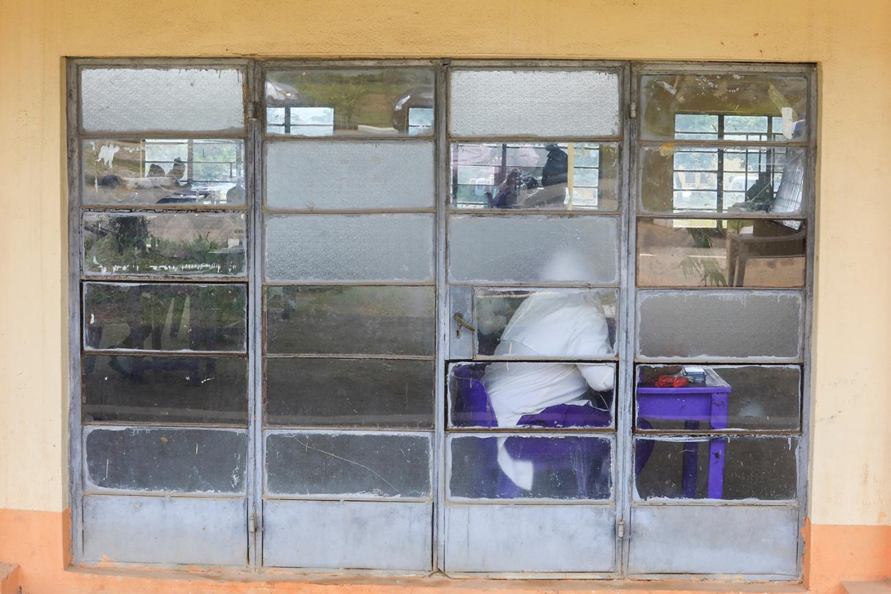 The photo shows a test taker in full protective gear inside a classroom in a picture taken from outside. 