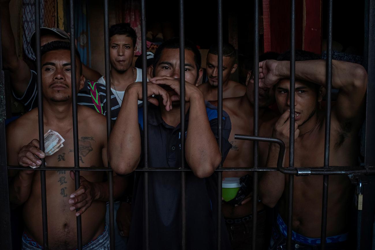 The photo shows a crowded cell of men looking out of their prison cell. 