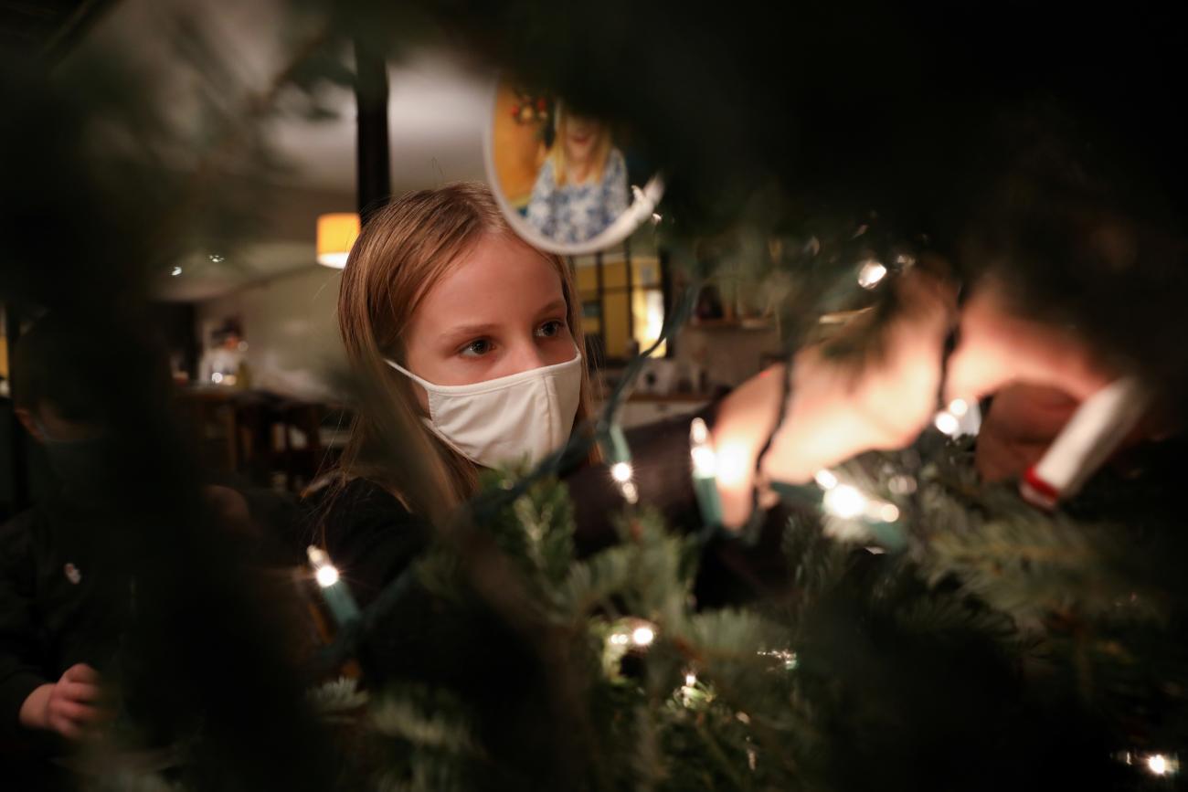 A young girl decorates her Christmas tree while wearing a face mask as a precautionary measure, as the global outbreak of the coronavirus disease continues in New York City on December 6, 2020. 