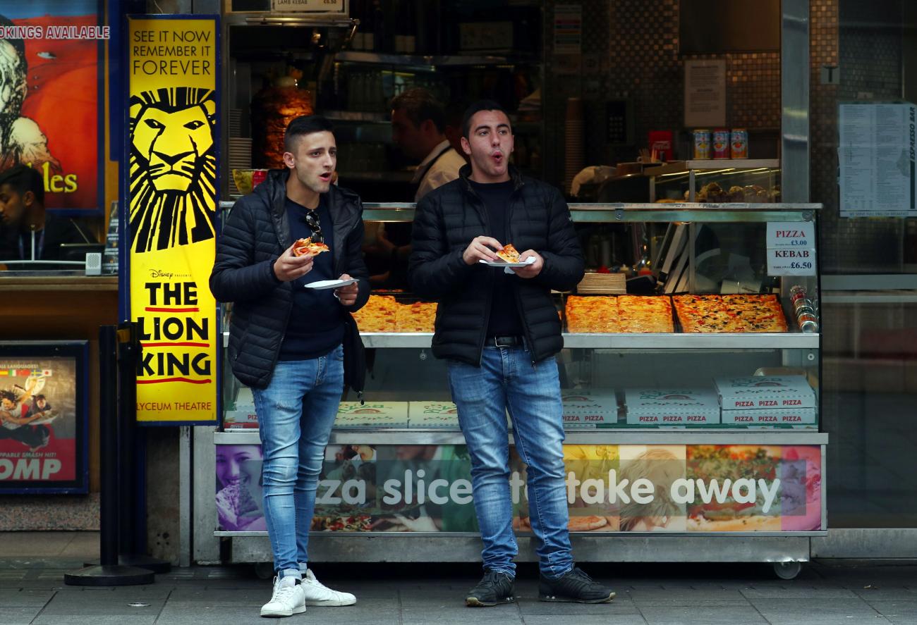 Customers eat pizza slices in front of a fast food outlet in central London, Britain, on September 25, 2017.