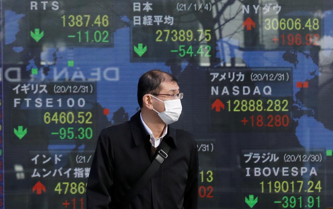 A man wearing a facial mask, following the coronavirus disease (COVID-19) outbreak, stands in front of an electric board showing Nikkei (top in C) and other countries stock index outside a brokerage at a business district in Tokyo, Japan, January 4, 2021.