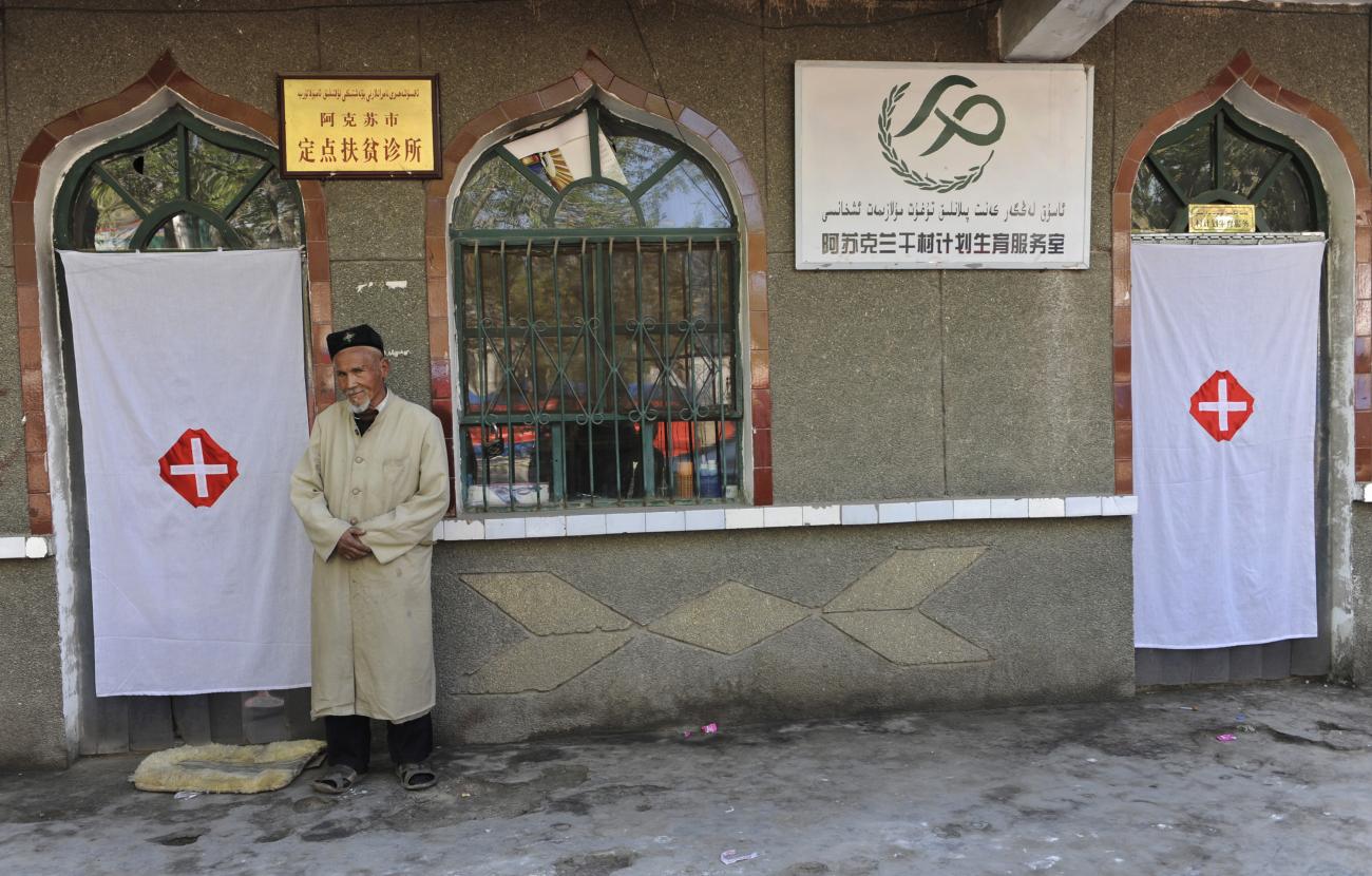 An elderly Uyghur man stands near the entrances to a medical clinic for the poor and a service room for birth control, in Aksu, Xinjiang Uyghur Autonomous Region, on April 18, 2012.