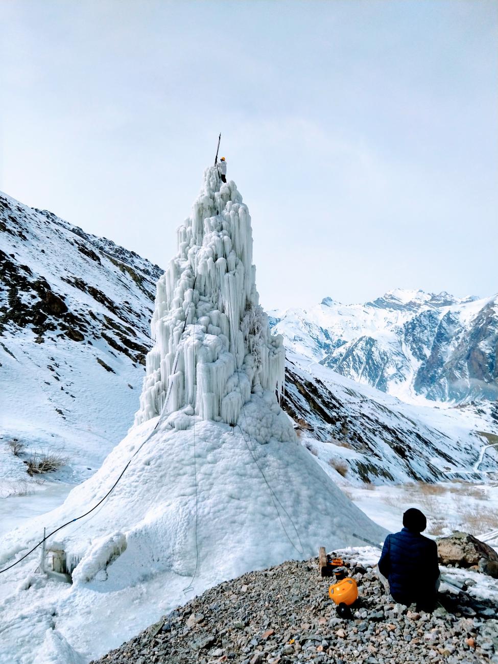 A hiker sits in front of an ice stupa in the Zanskar valley.