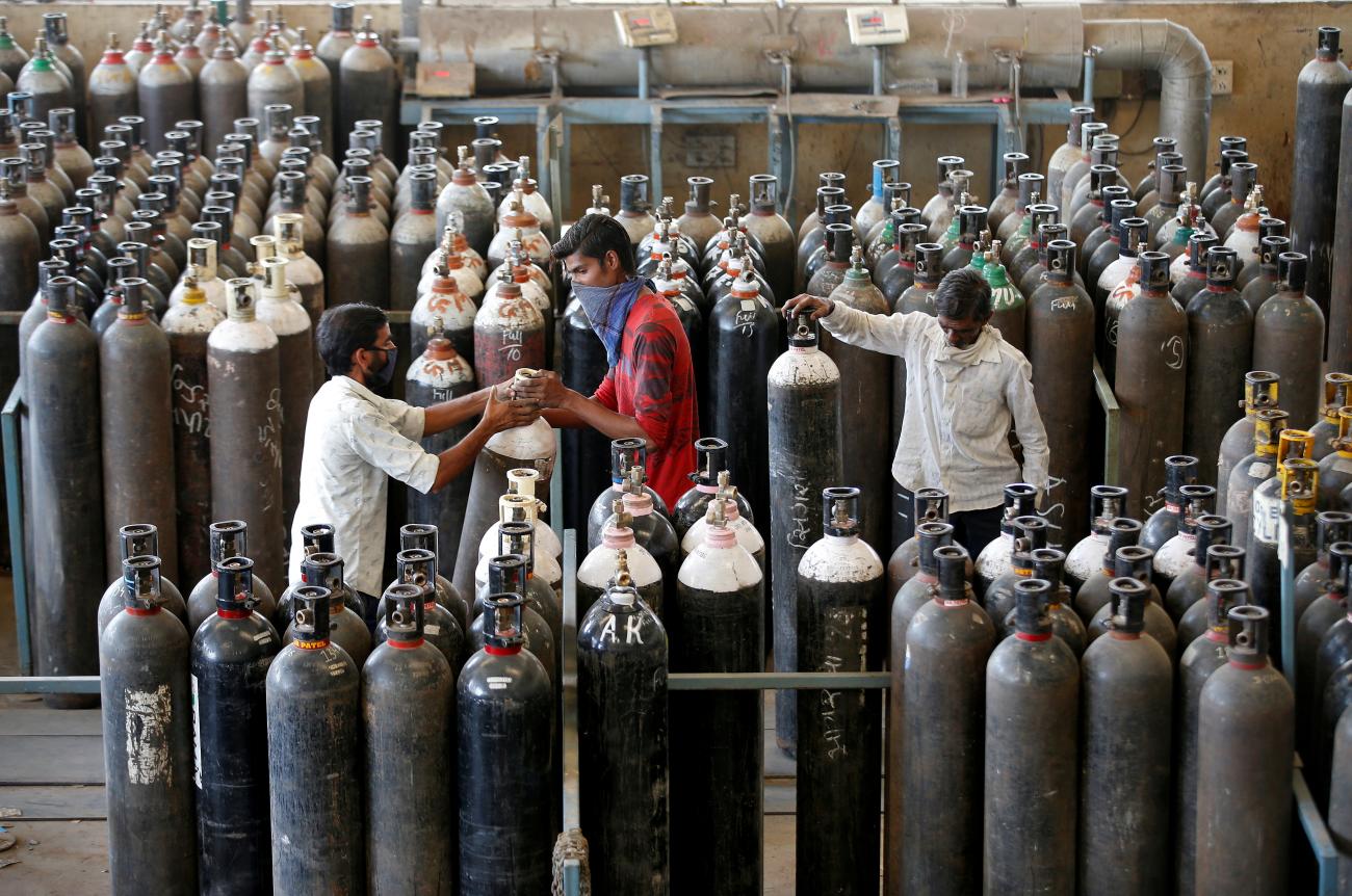 Thrree men stand among dozens of shoulder-high oxygen cylinders after refilling them in a factory in Ahmedabad, India, on April 25, 2021. REUTERS/Amit Dave