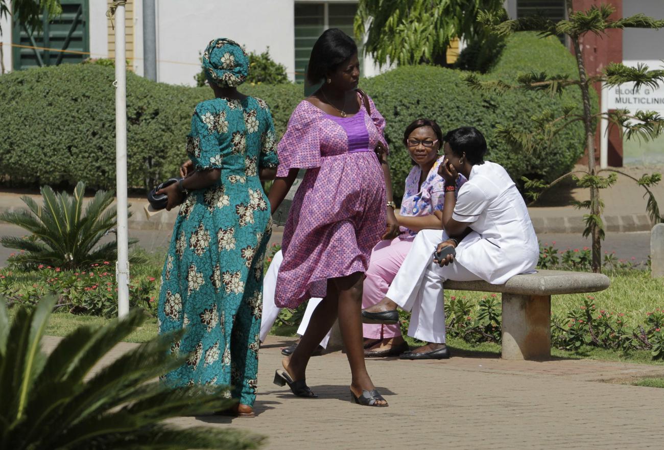 A pregnant woman in a purple dress walks past health-care workers at the National Hospital Abuja, in Abuja, Nigeria, on March 5, 2013. 