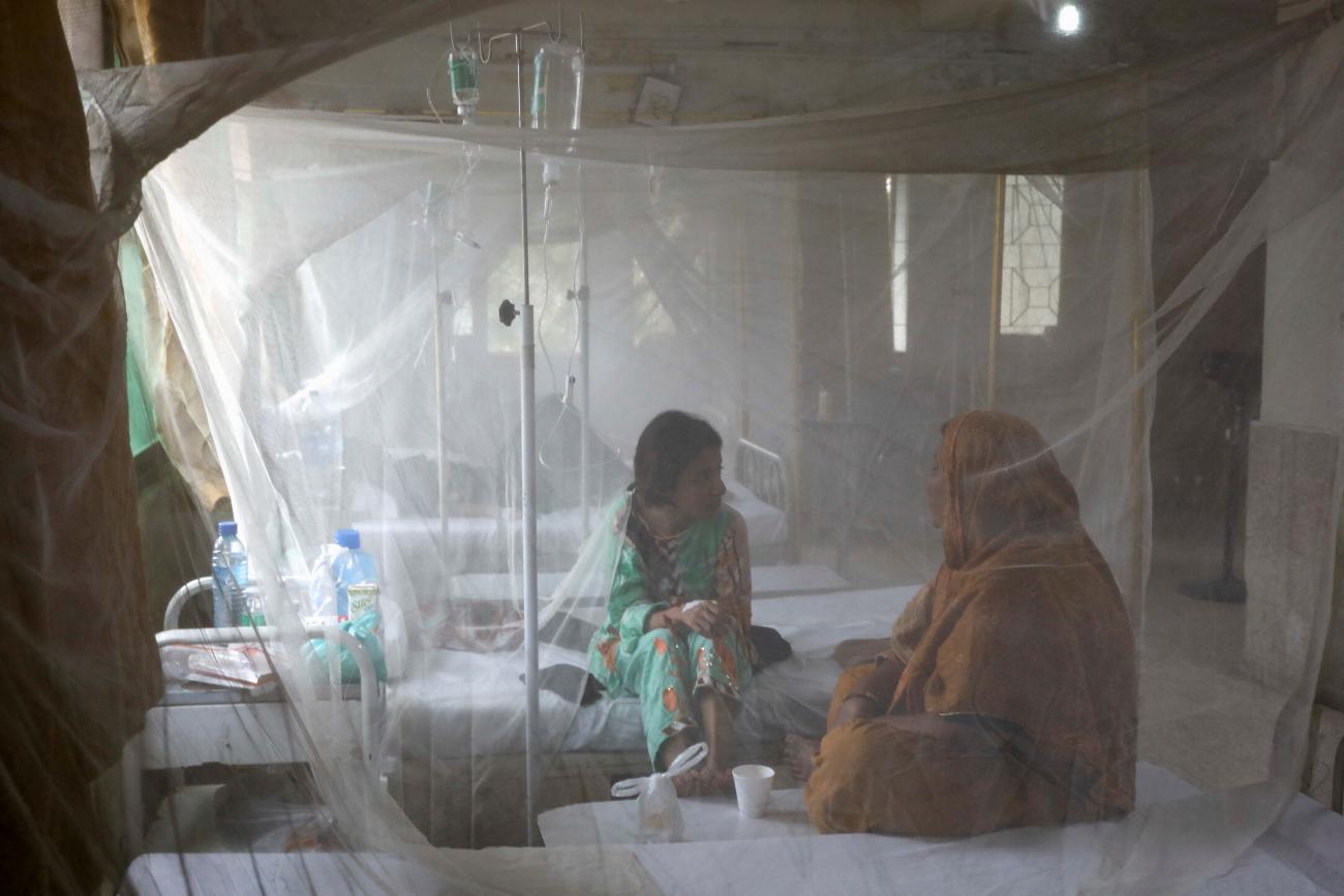 A patient suffering from dengue fever chats with a woman while sitting under a mosquito net inside a dengue and malaria ward at the Sindh Government Services Hospital in Karachi, Pakistan, on September 21, 2022. REUTERS/Akhtar Soomro