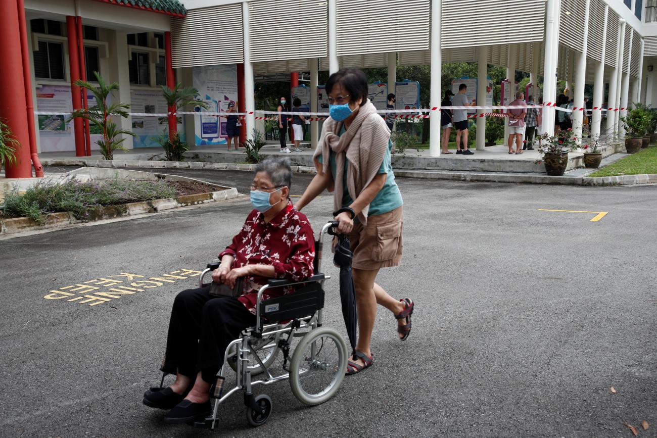 A person pushes a wheelchair-bound voter at a polling station during a time band allocated to seniors and elders.
