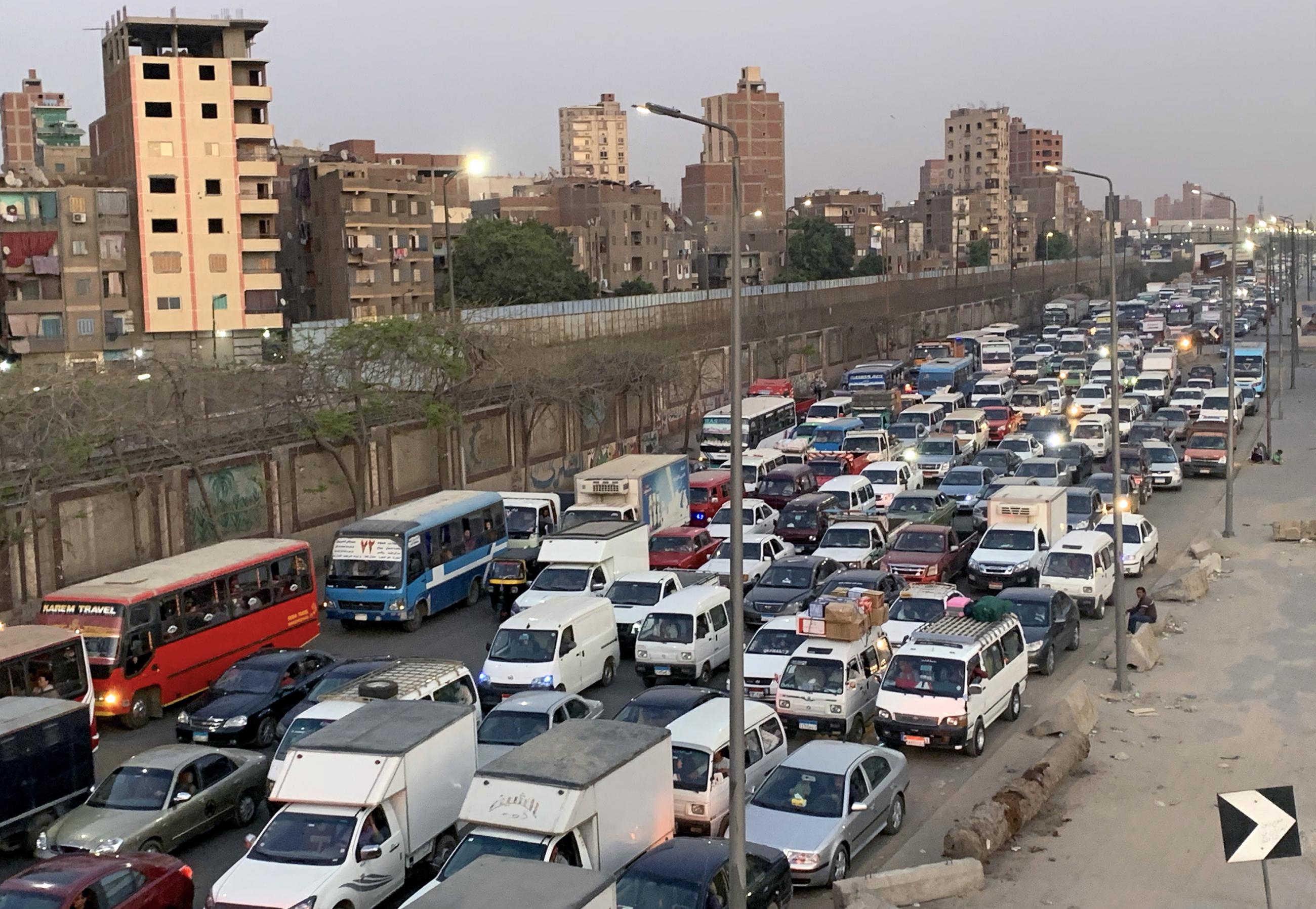 The photo shows a dusty street packed with cars and trucks. 
