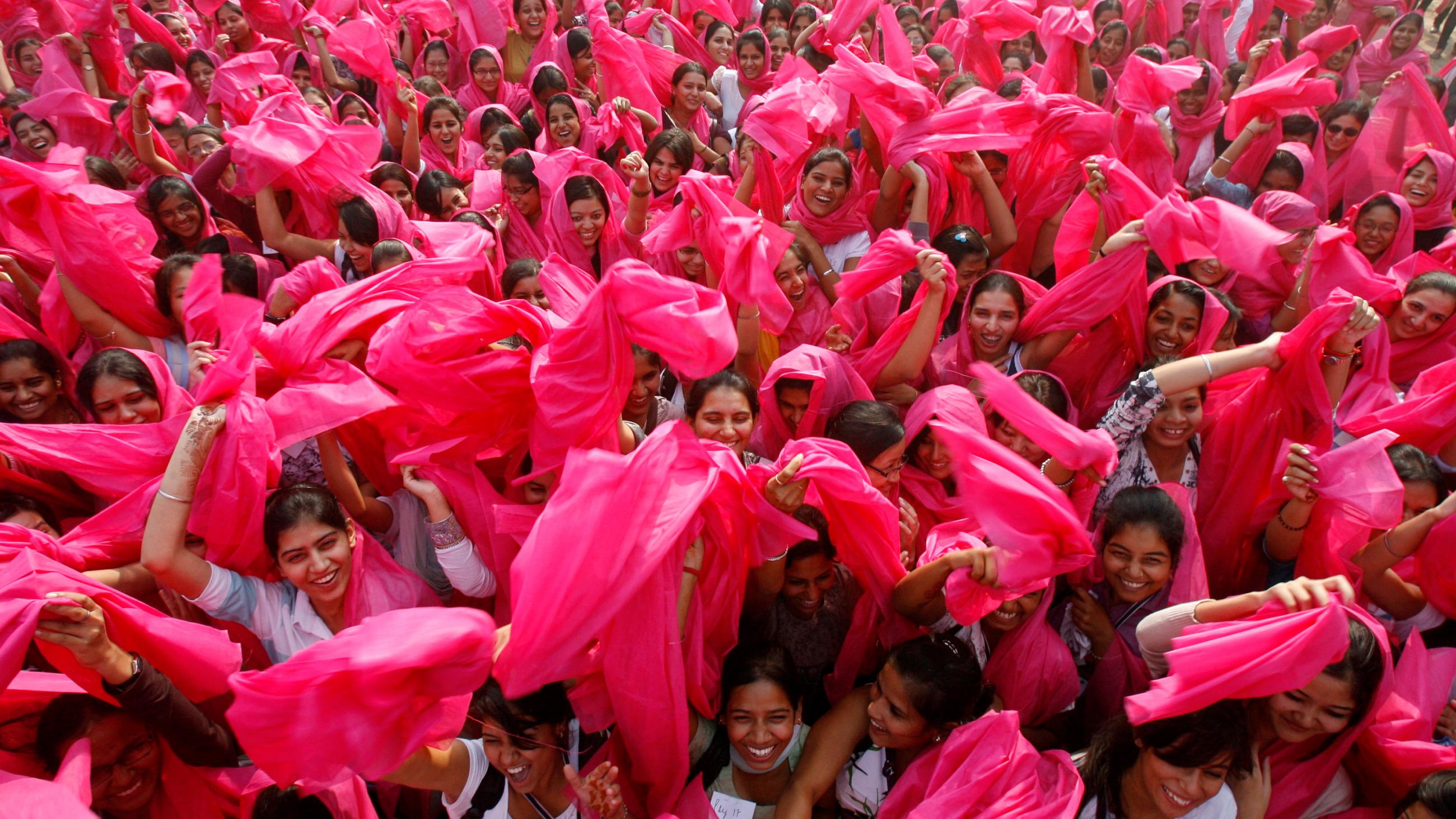 The photo shows a large crowd of women waving pink scarves. 