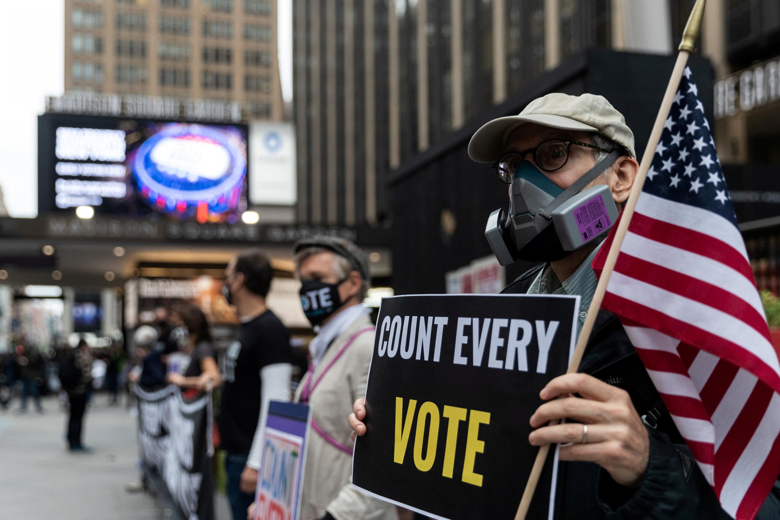 An older man wearing a respirator-style protective mask due to COVID-19 pandemic holds a sign outside Madison Square Garden, which is used as a polling station, on the first day of early voting in Manhattan, New York.