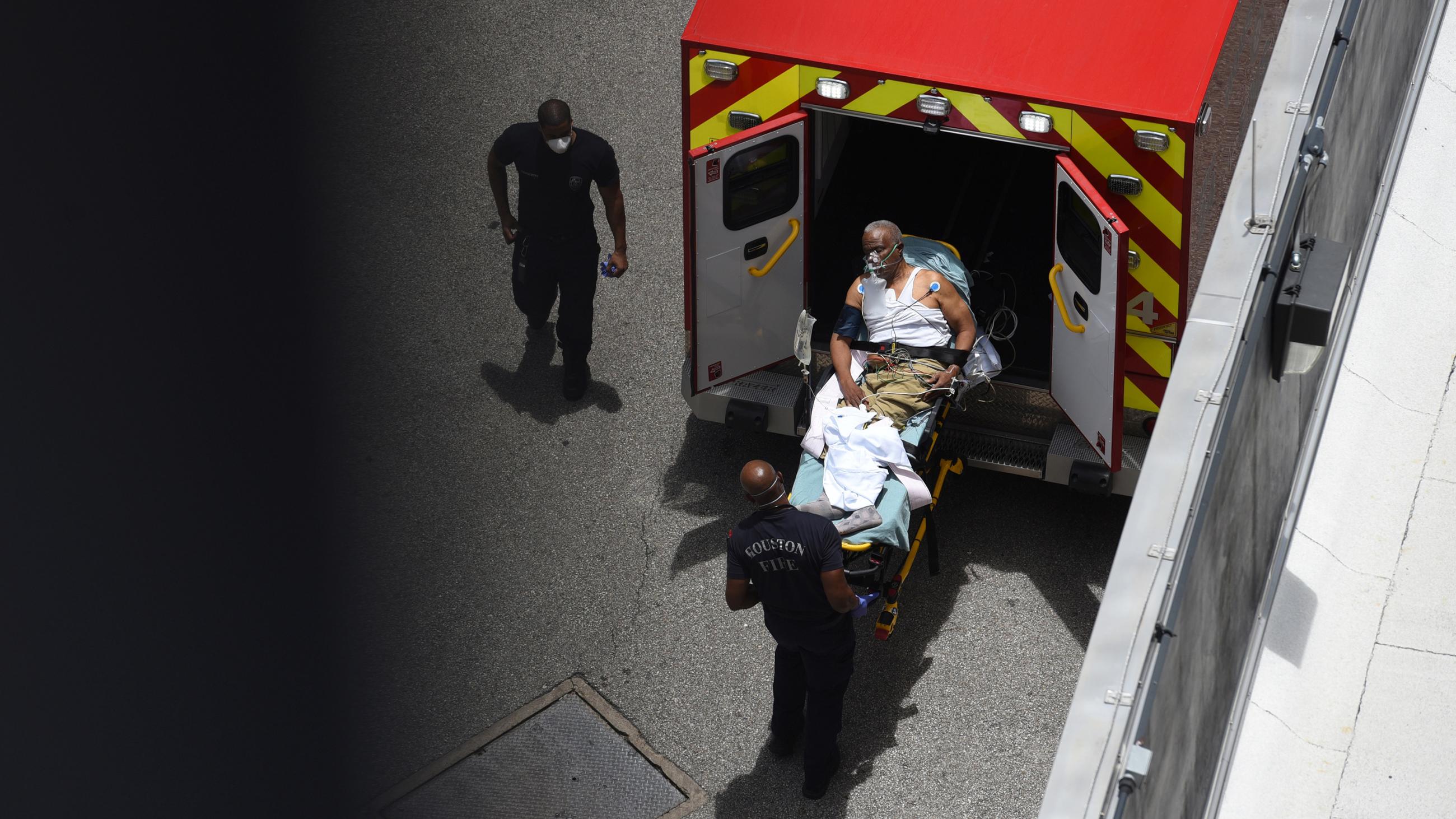 The photo shows a person on a gurney being taken out of the back of an ambulance in a picture captured from above. 