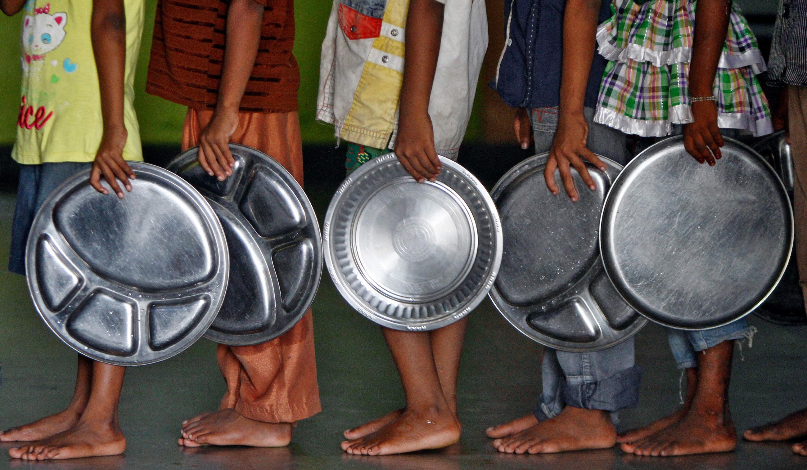 The photo shows a long line of people holding large metal platters. 