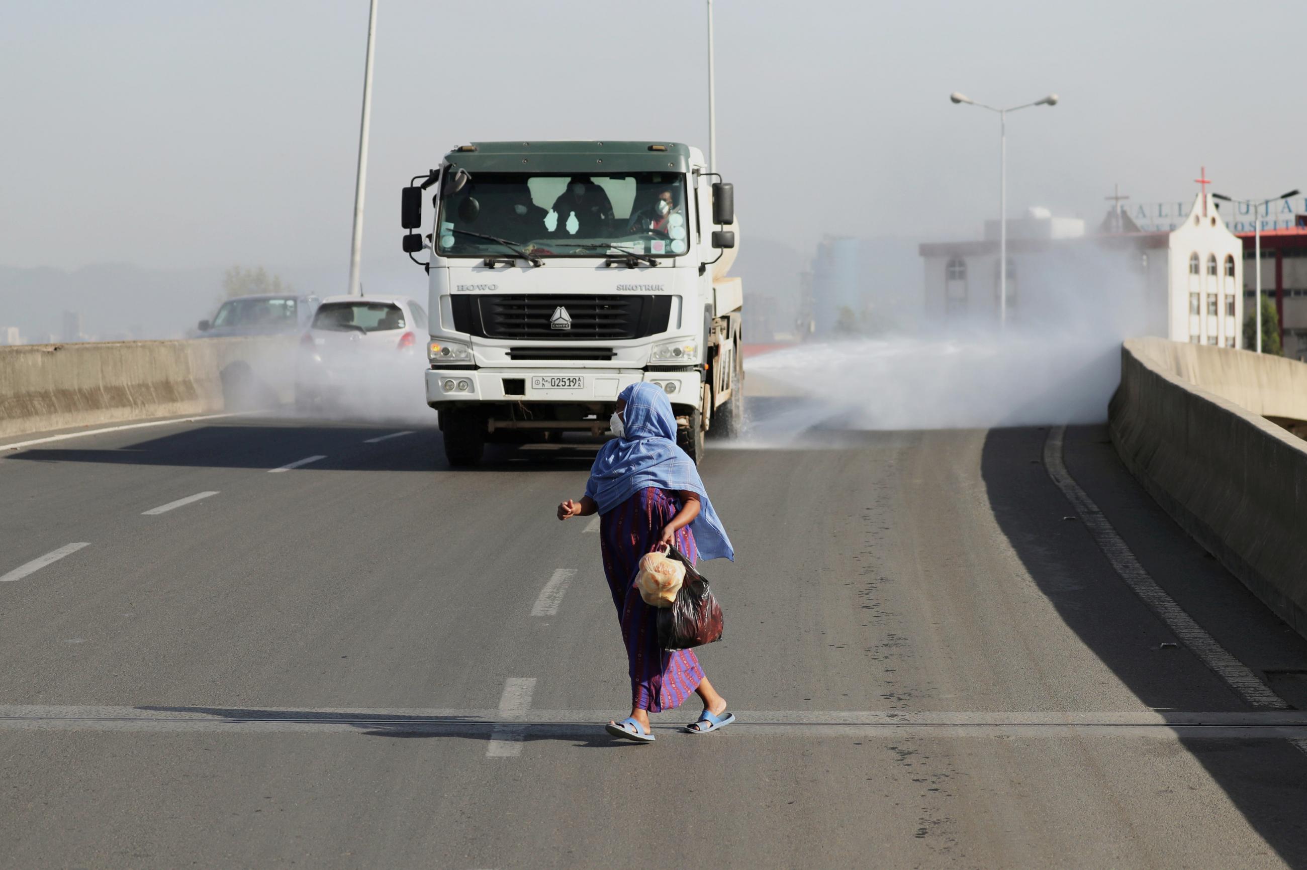 A woman wearing a face mask, runs in front of a truck spraying disinfectant on the street as part of measures to prevent the spread of COVID-19 in Addis Ababa, Ethiopia on March 29, 2020.