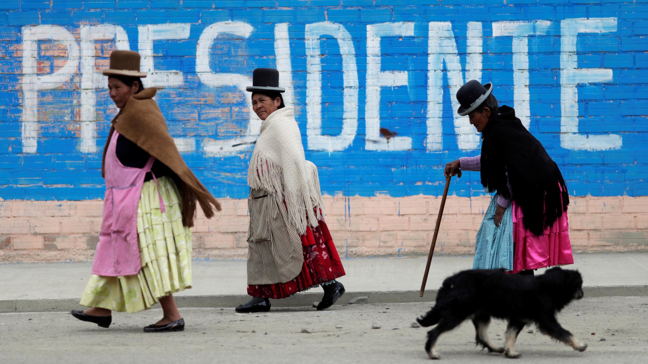 Older Bolivian women walk past wall art that reads, "Presidente," after voting at a polling station during the presidential election in La Paz, Bolivia, on October 18, 2020.