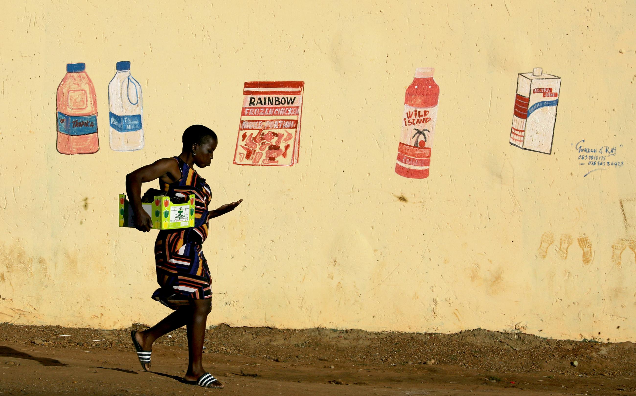 A woman counts her change as she leaves a convenience store, or "spaza shop", with a mural depicting grocery items, during a nationwide lockdown for 21 days to try to contain the coronavirus disease (COVID-19) outbreak, at the Elias Motsoaledi informal settlement, South Africa, April 7, 2020. 