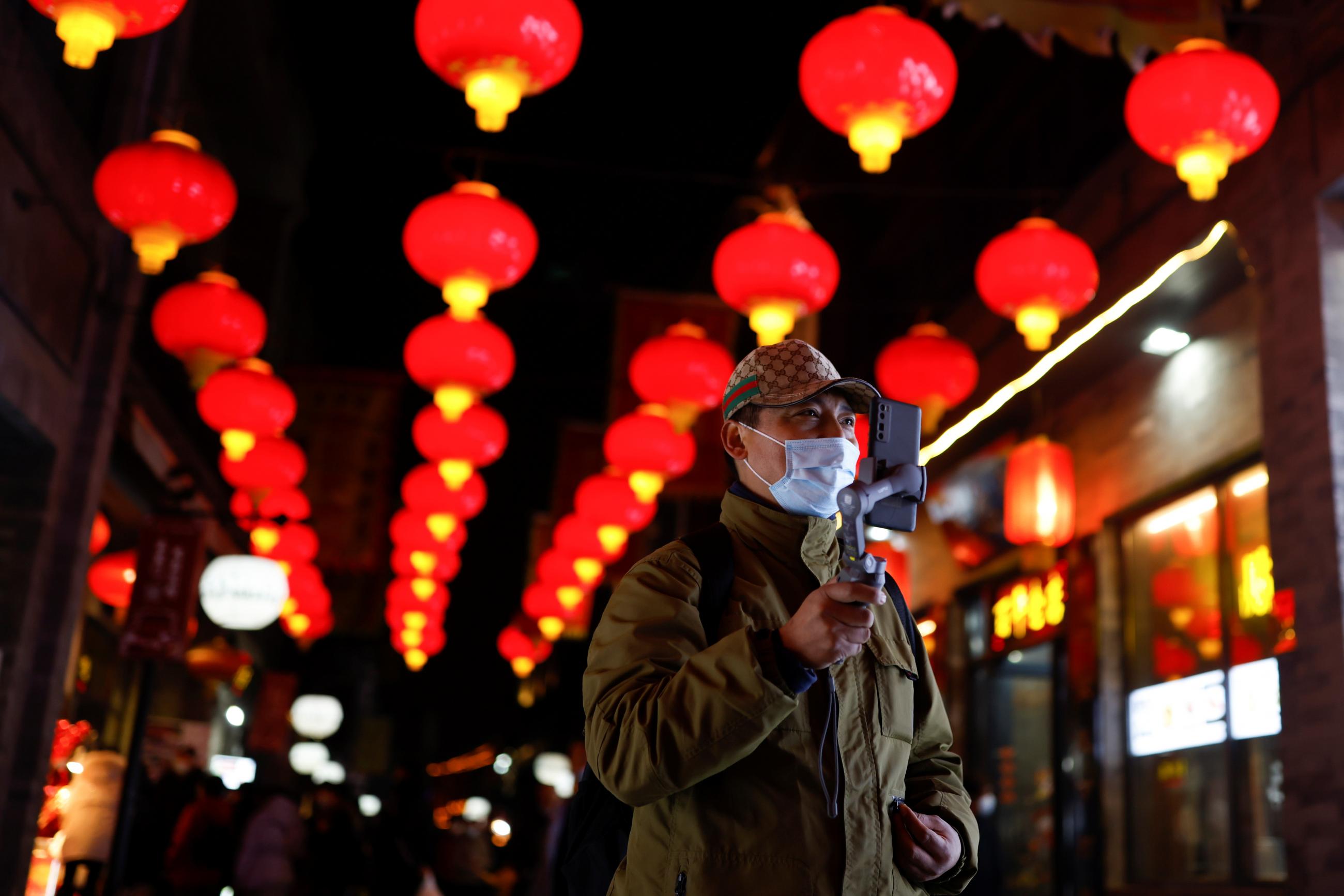 A man wearing a face mask following a COVID outbreak uses his phone while walking near lantern-lined Qianmen Street ahead of Lunar New Year celebrations, in Beijing, China on February 10, 2021.