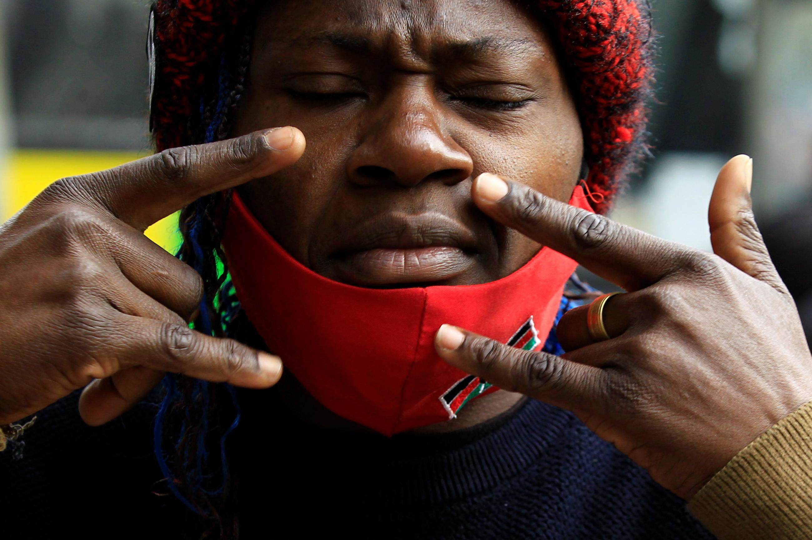 Deaf hawker Mercy Ayuma uses a sign language gesture, meaning the wearing of a face-mask to control the spread of coronavirus disease (COVID-19) pandemic, next to her open-kiosk at the Kencom bus terminus in downtown Nairobi, Kenya