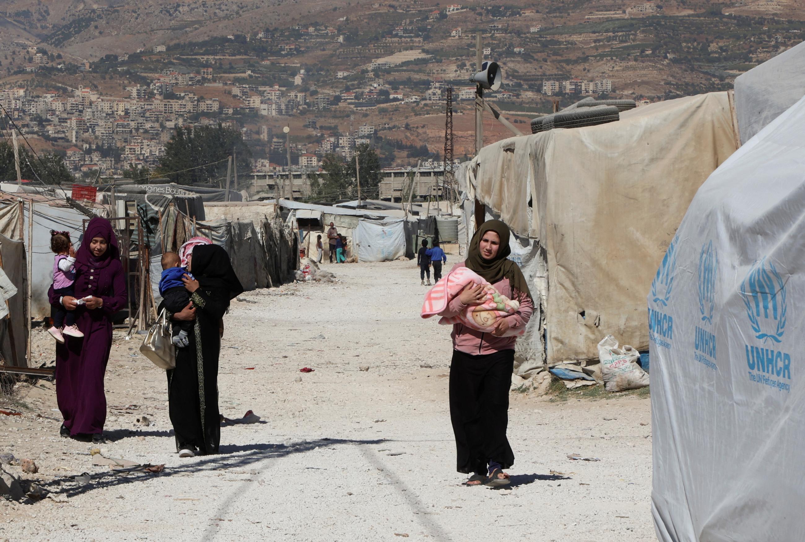 Syrian refugee women carry children as they walk at an informal camp, in the Bekaa Valley, Lebanon October 18, 2022.