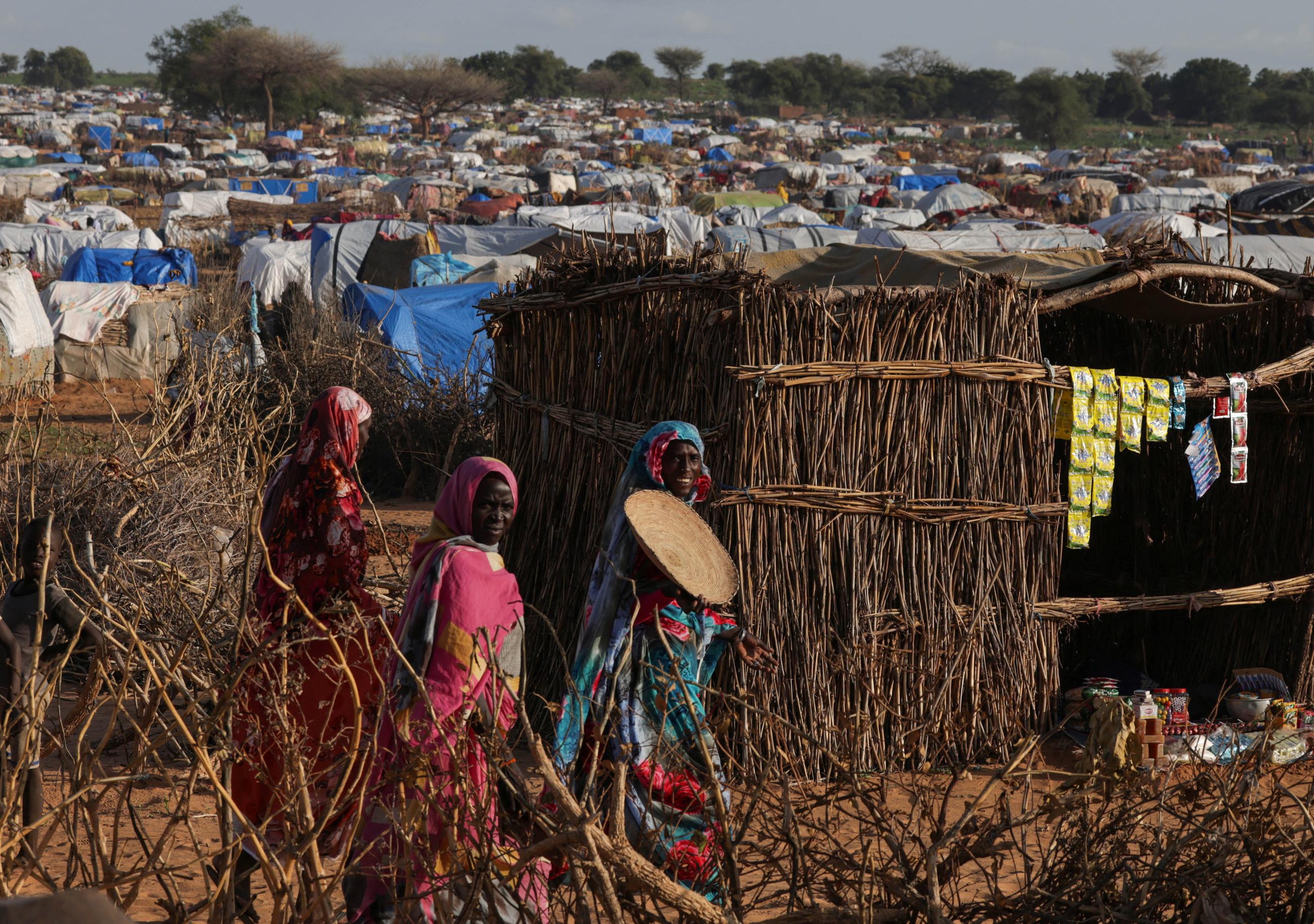 Sudanese women, who fled the conflict in Geneina in Sudan's Darfur region, walk beside makeshift shelters.