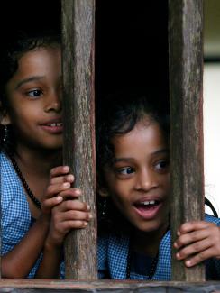 The picture shows twin girls smiling as they peek out the window. 