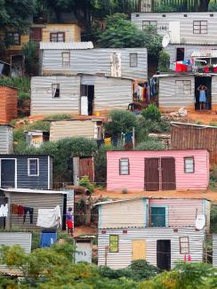  The photo shows a hillside covered with tin shacks, some colorfully painted. 