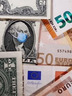 The photo shows a bunch of paper money, dollars and euros, with a blue surgical-style mask on one of the bills. 