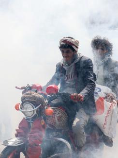 This is a powerful photo showing two men on one motorbike driving through a thick cloud of disinfectant mist. 