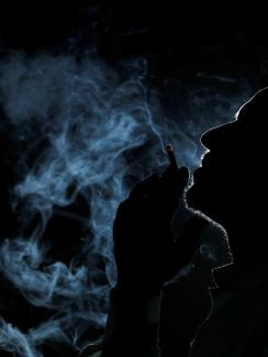 The image shows a dark silhouette of a man in profile smoking and filling the air around him with smoke. 