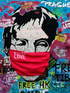 The photo shows a large graffiti mural of the legendary singer and peace activist with a mask draped over Lennon's face. A man in the foreground holds his device at arm's length taking a selfie. 