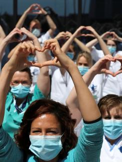 The photo shows a large number of health workers standing together and holding up a heart symbol above their heads. 