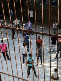 The photo shows a large crowd of people from behind the bars of an iron fence. 