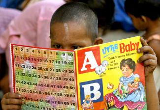 A boy with a shaved head reads an ABCs learning book with a yellow cover