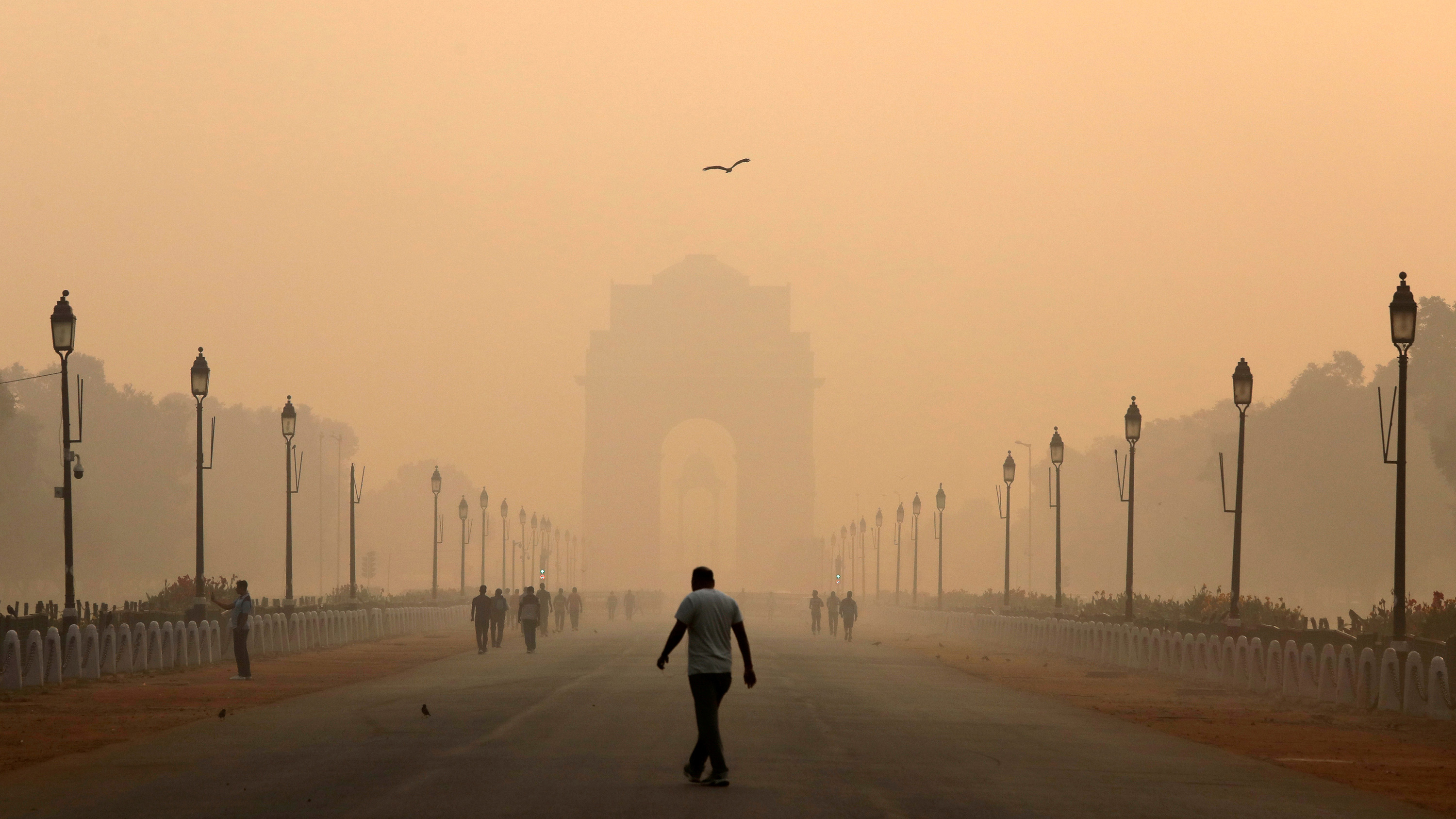 Photo shows a man in the distance and a grand architectural structure in the far distance, which is hard to see through the smog.