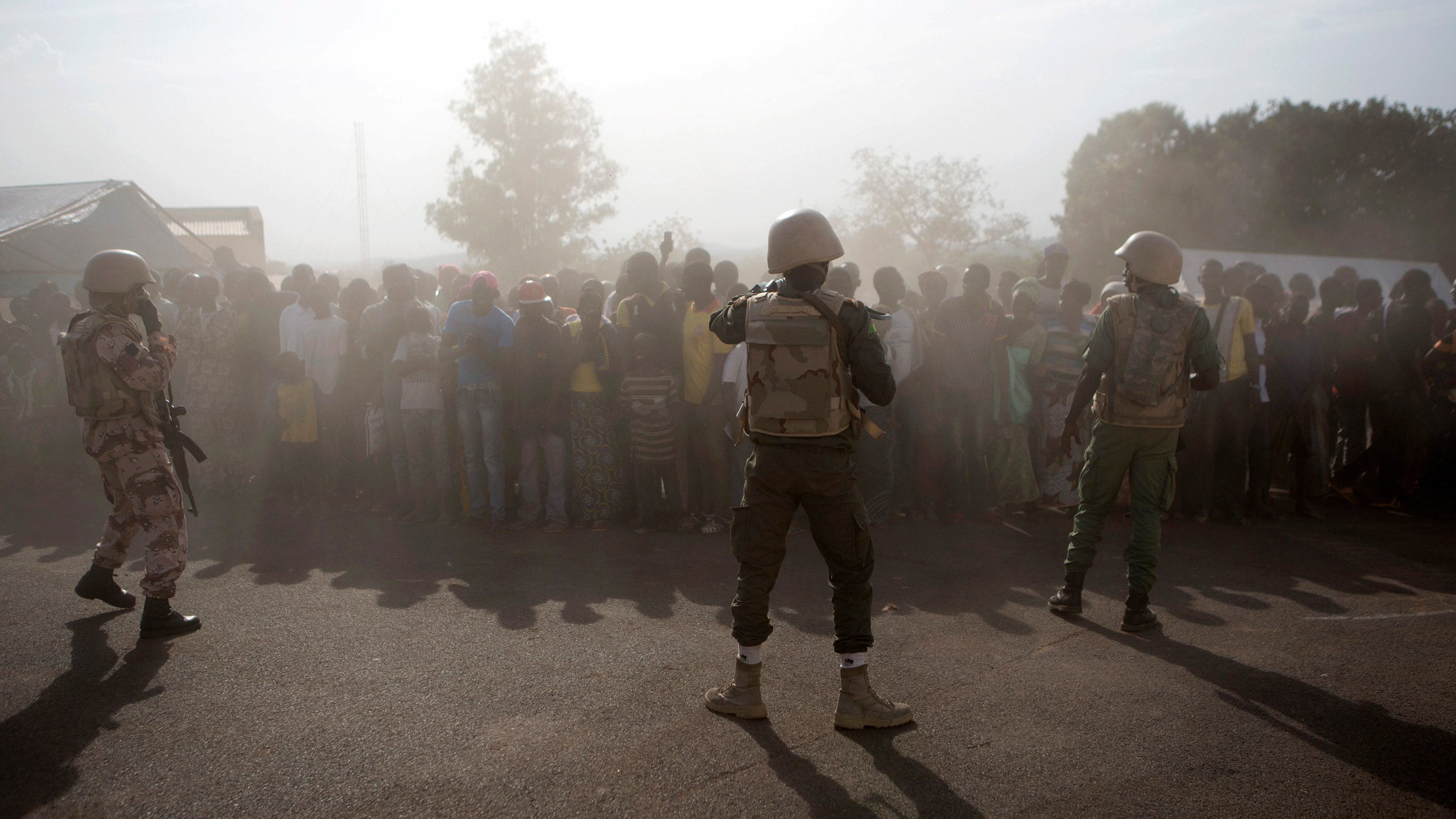he picture shows a large crowd shrouded in what appears to be early morning mist with a thin line of heavily armed soldiers wearing combat fatigues standing between them and the camera.