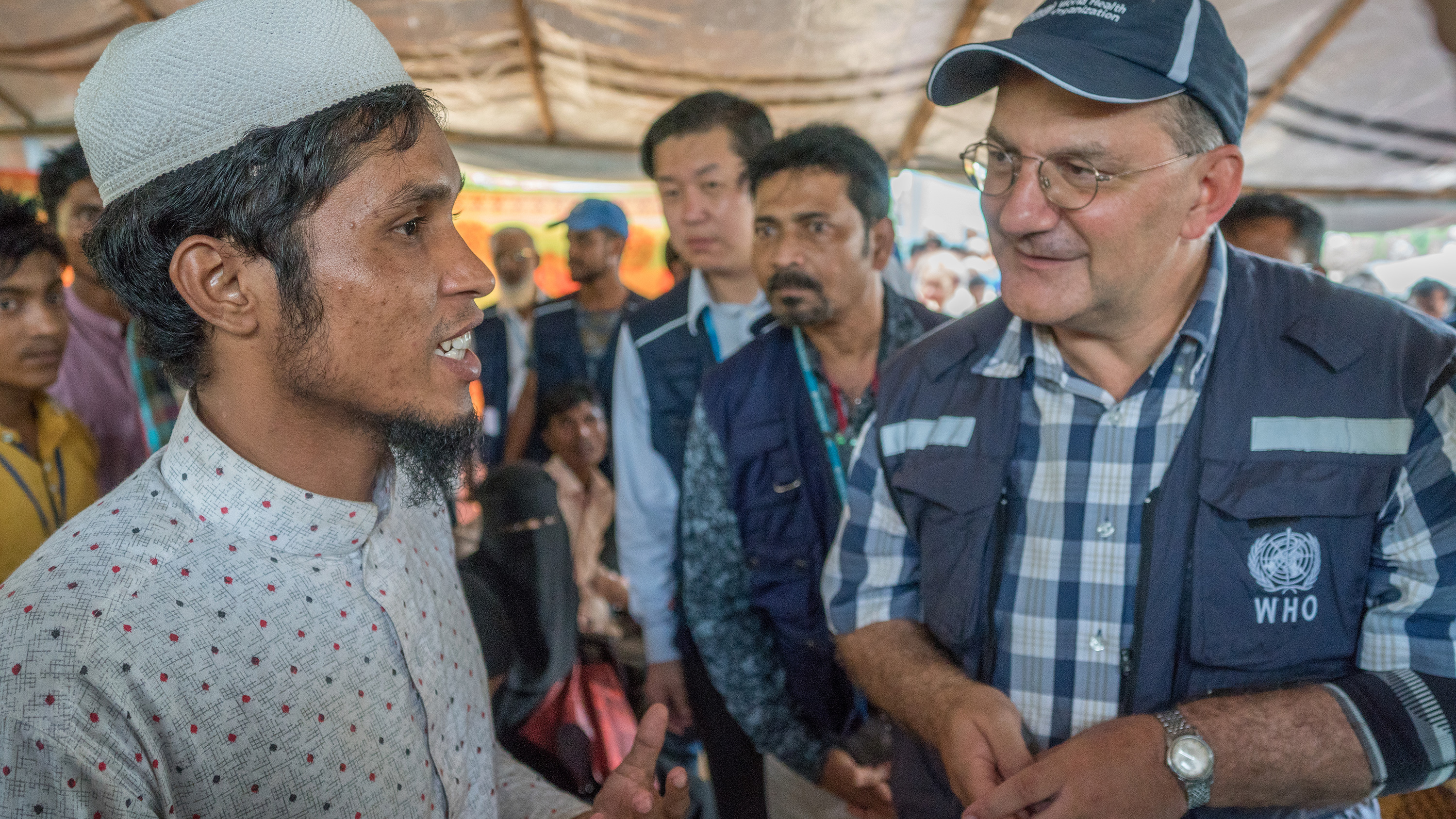 Photo shows Dr. Salama speaking to one individual in a covered area filled with people.
