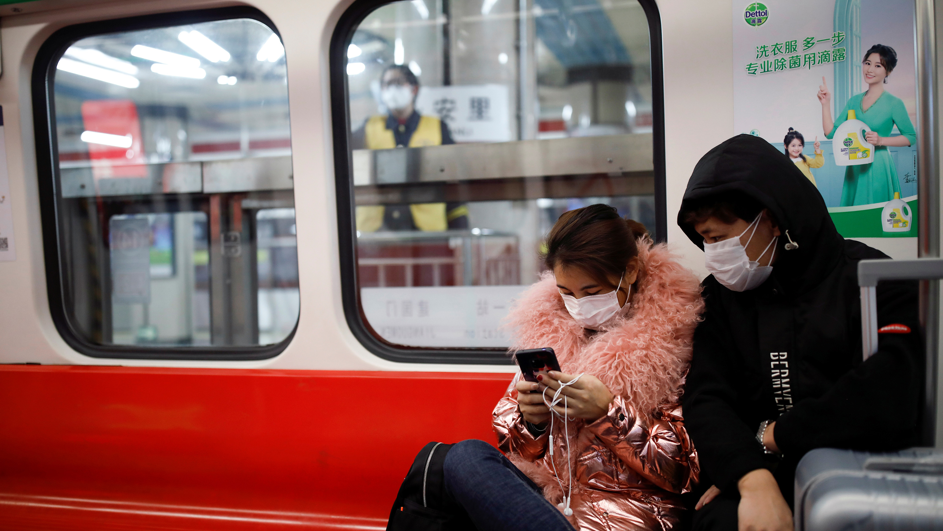 The image shows two people sitting close to each other. She wears a shiny, puffy metallic pink winter coat and he wears a simple black hoodie pullover. She is on her device, and he is looking over her shoulder.