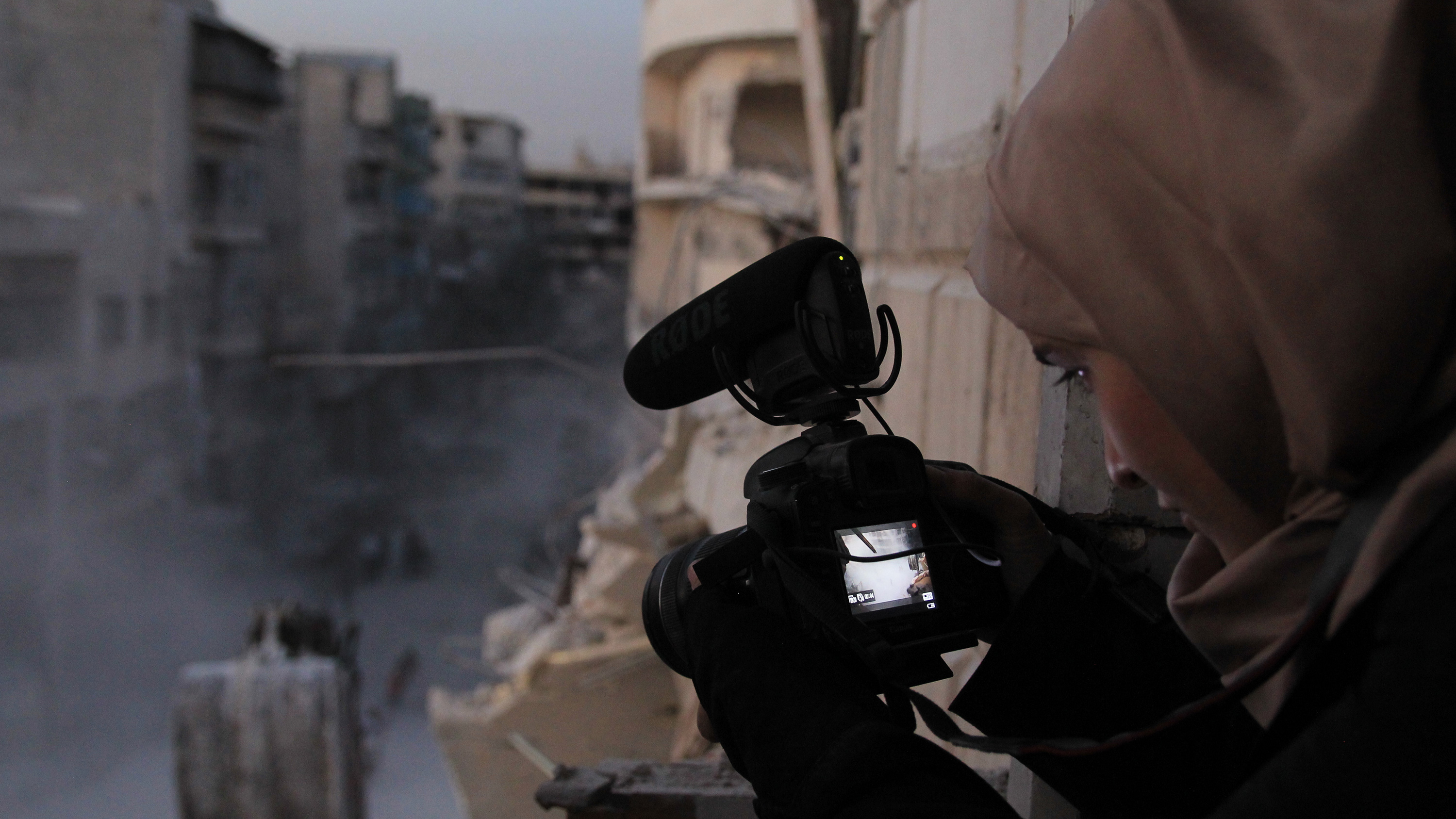 The picture shows the filmmaker from behind, as she captures a view of destruction from a high vantage overlooking the city street.