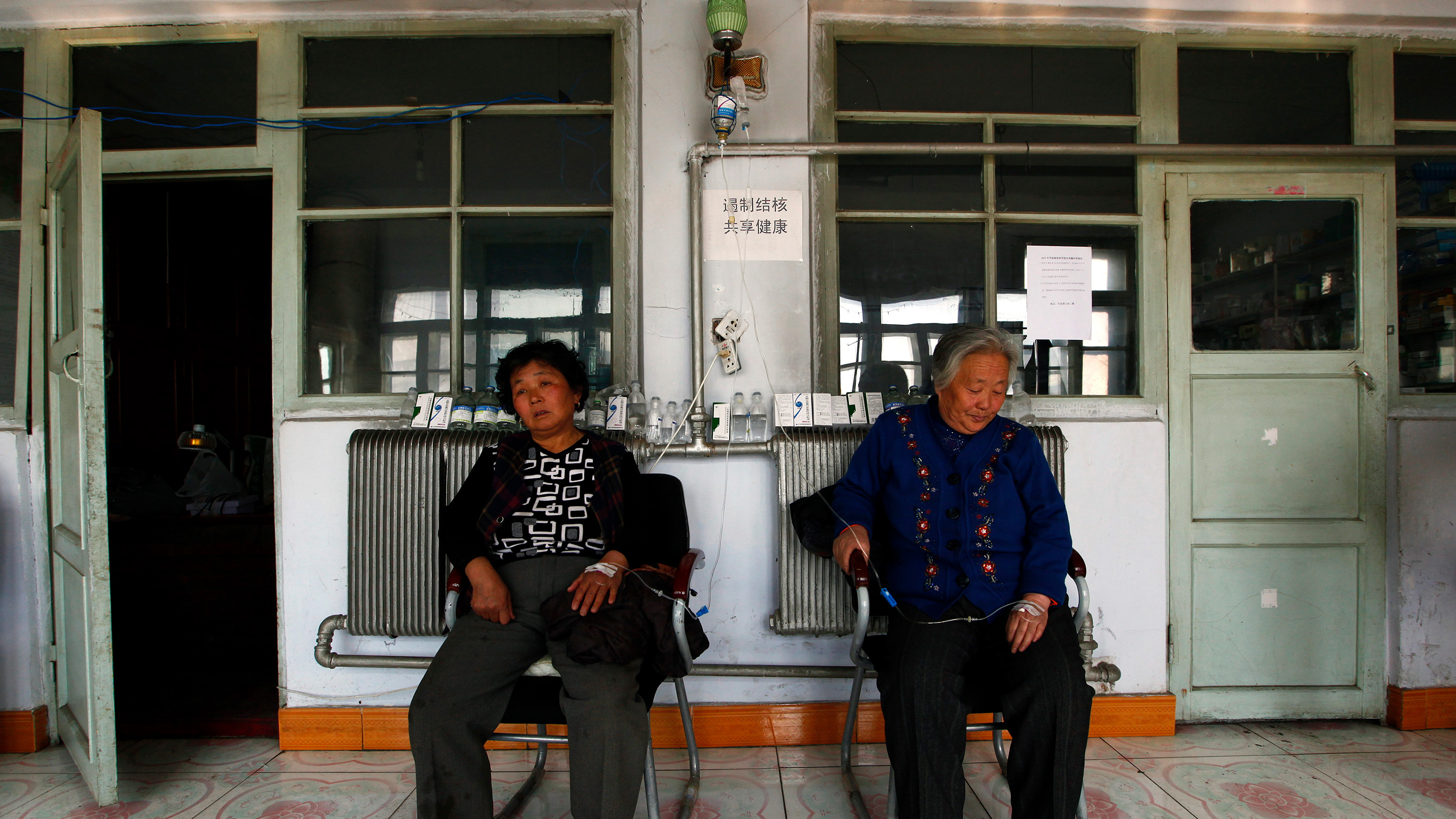 The picture shows two women seated with intravenous drips in their arms.