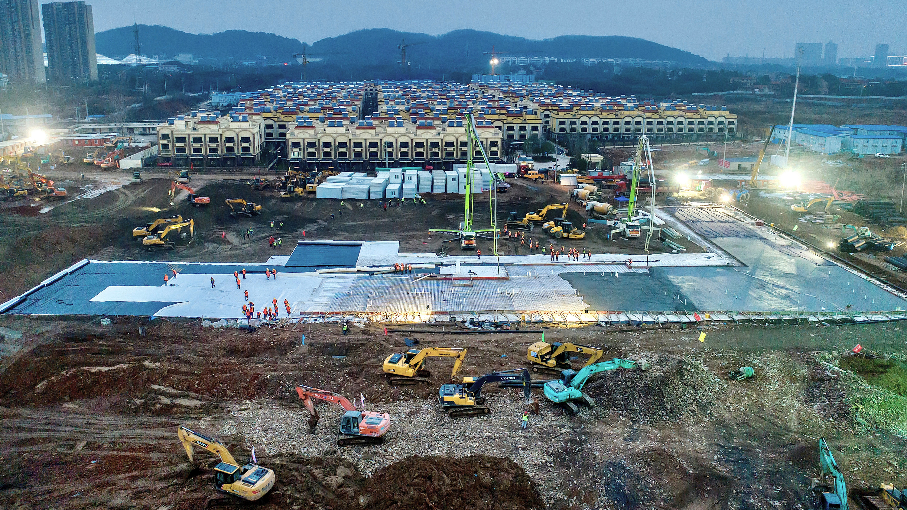 Picture is an aerial view of a massive construction site awash in activity with people and earth moving machines.