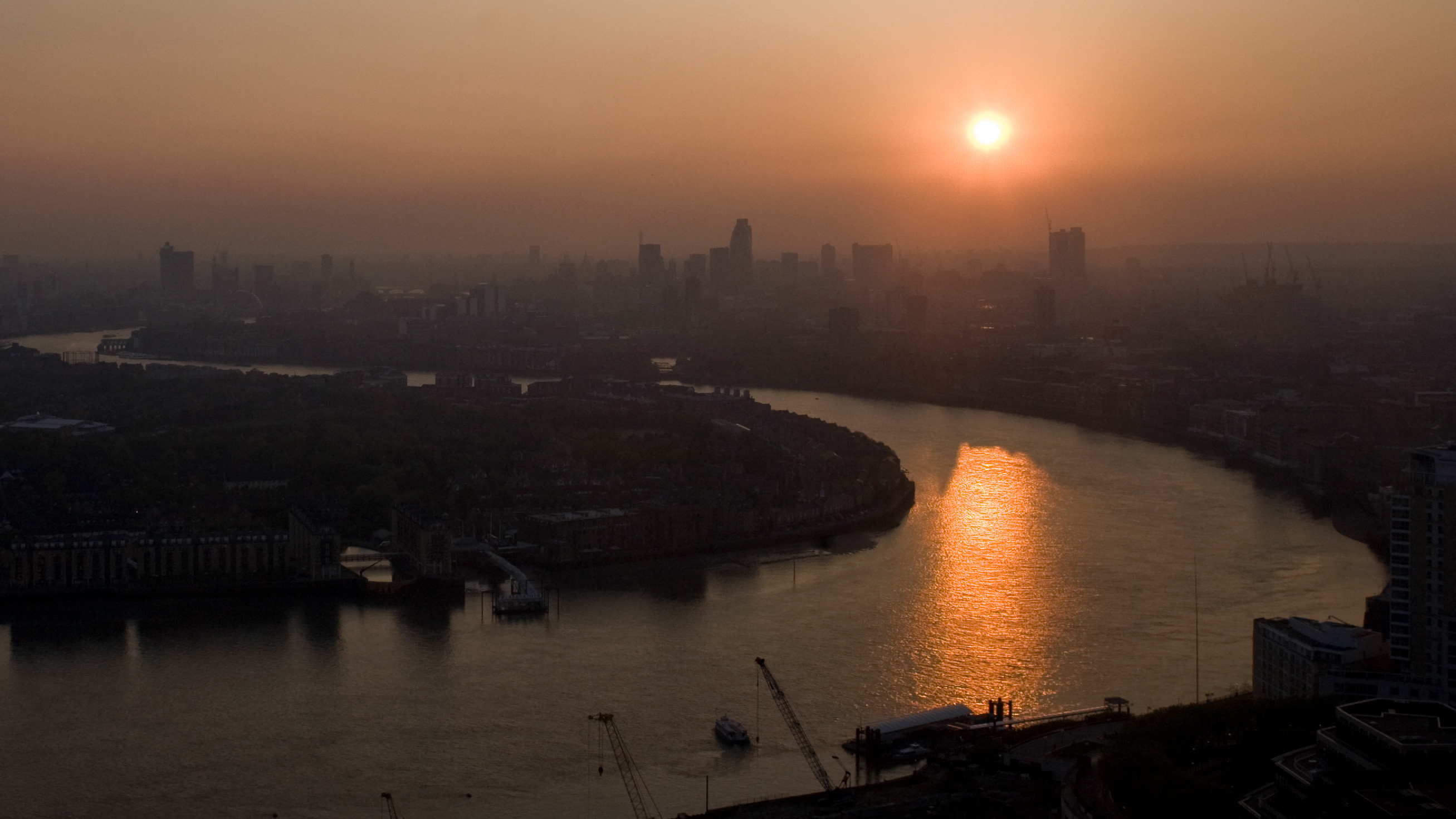 The picture shows a high angle shot of London at dusk with the sun setting over the Thames. Smog obscures buildings in the distance.