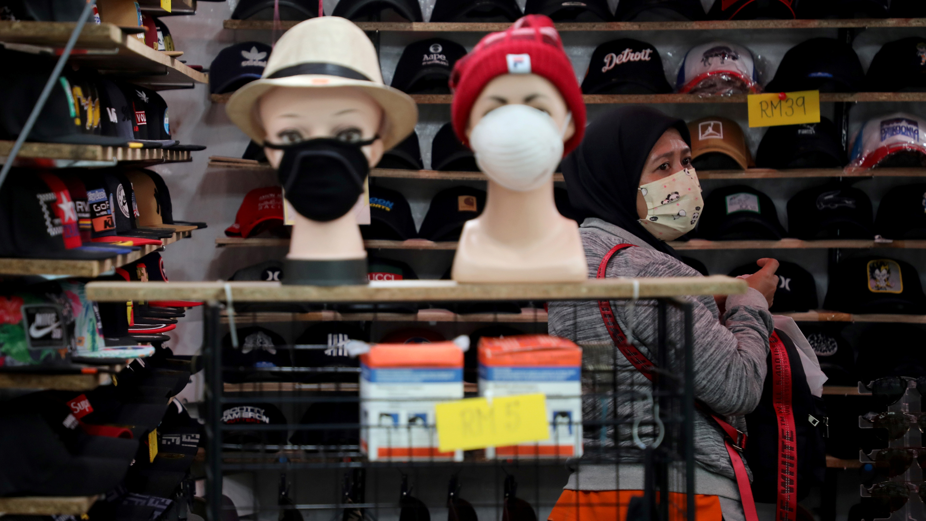 This is a striking photo showing a woman in a small shop selling hats and masks. She is herself wearing a mask.