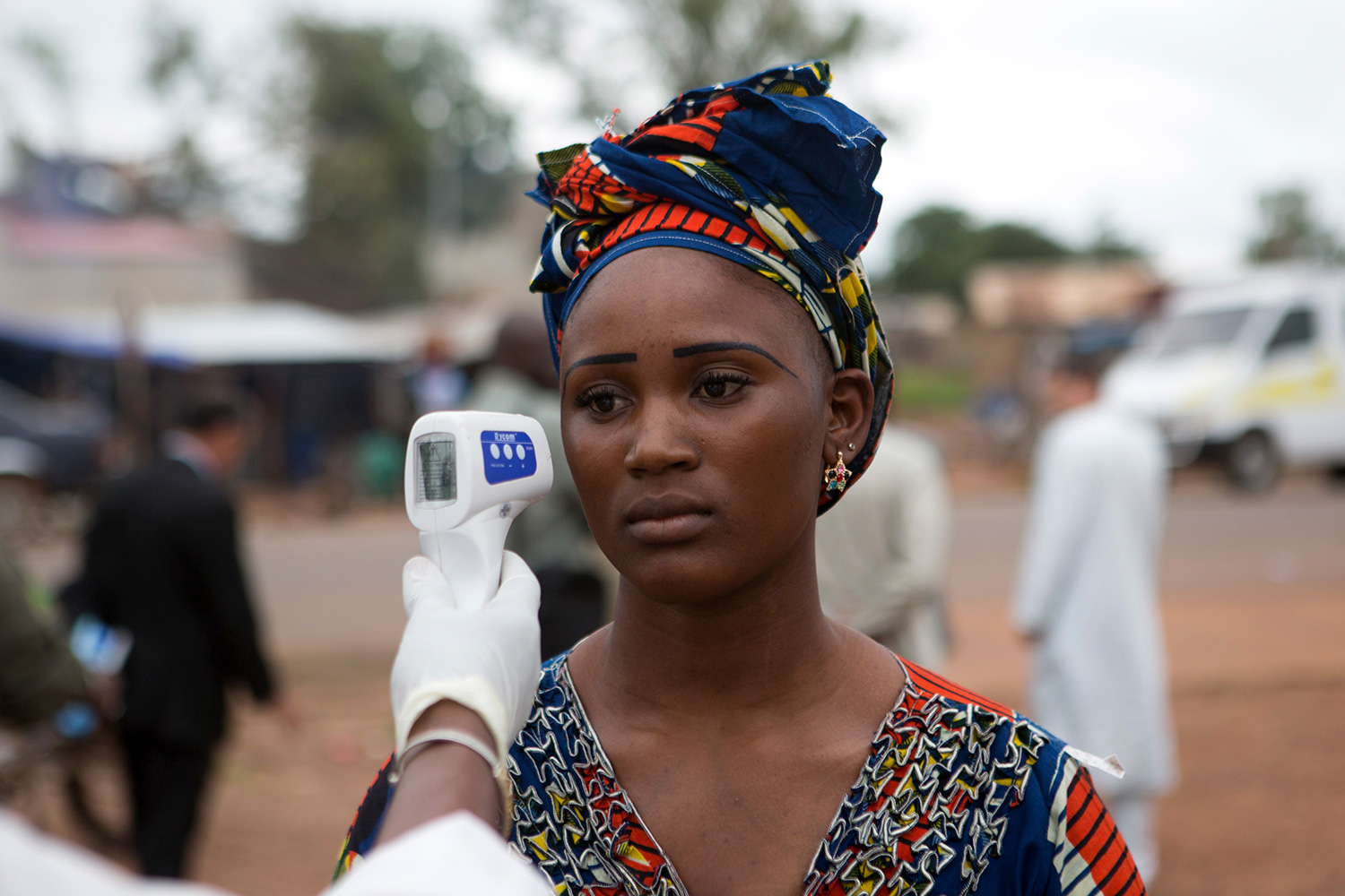 The picture shows a woman who is having her forehead scanned by a handheld device. She looks unhappy or tired.