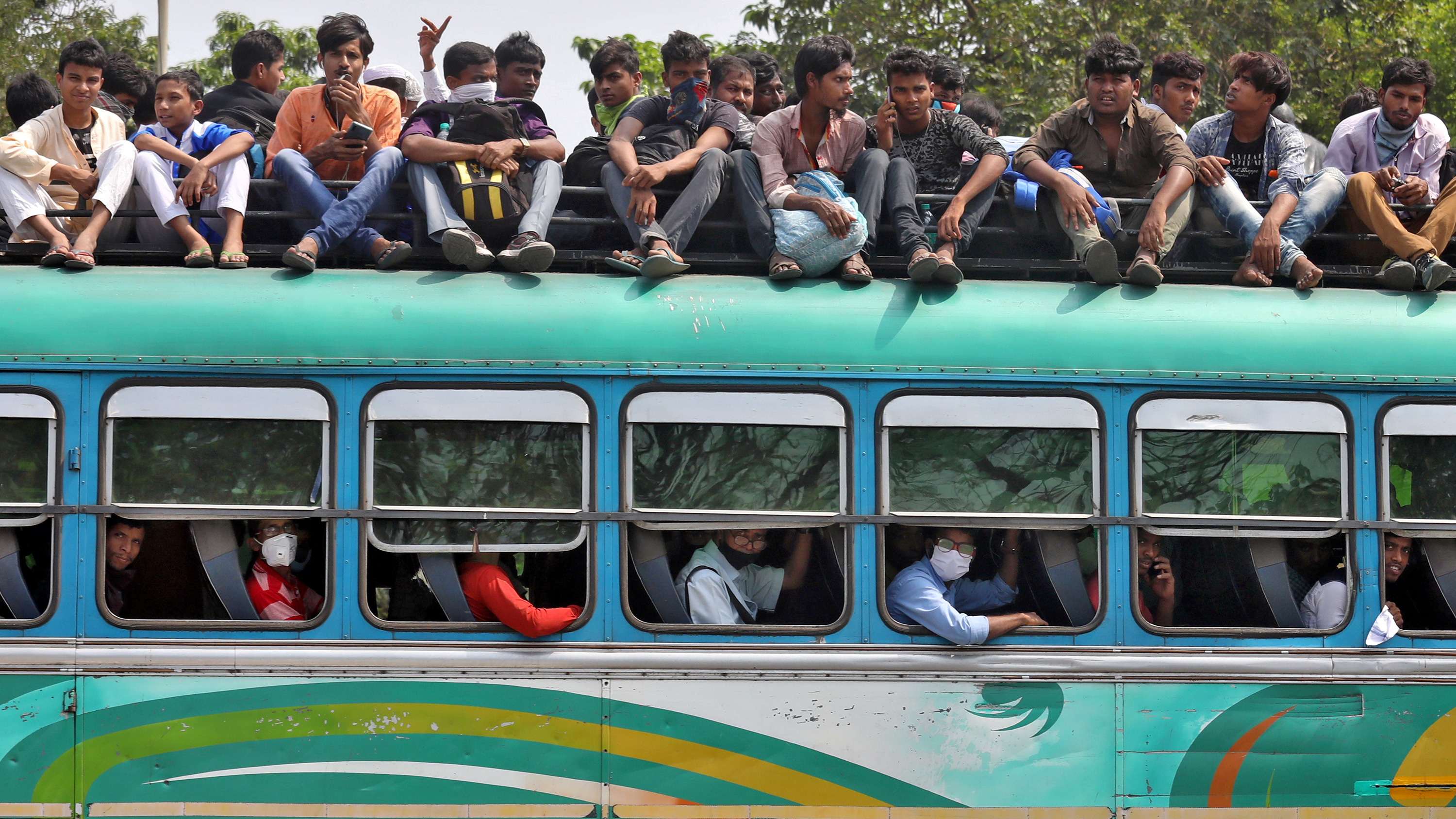 The image shows a green bus, its seats full, with many people sitting on top of the vehicle.