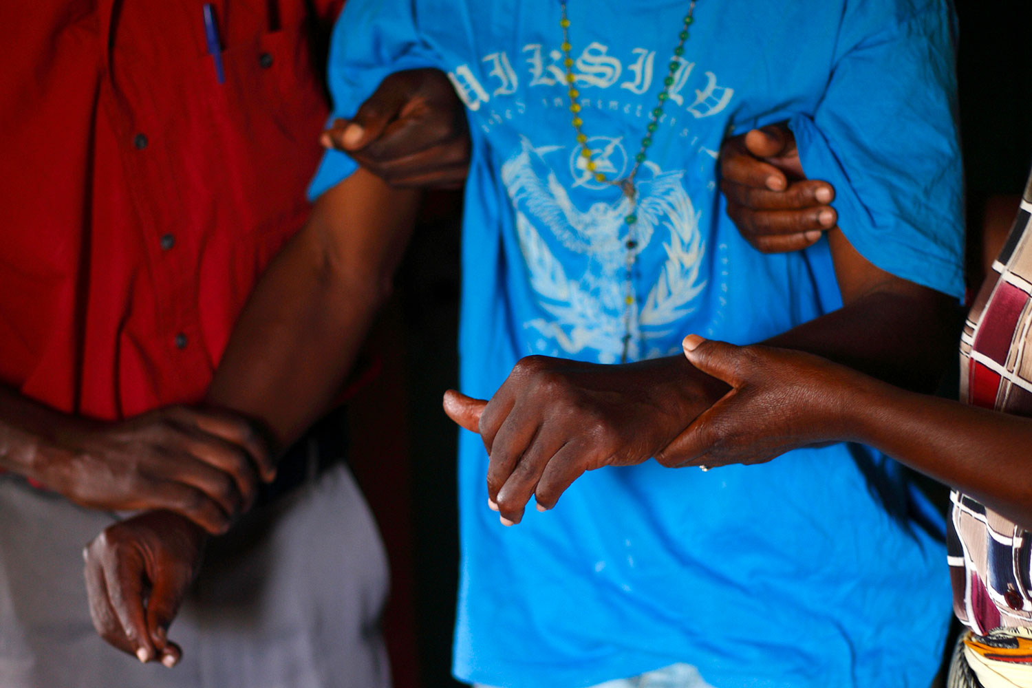The picture shows the torso of a man wearing a loose-fitting light blue shirt being helped by two other people.