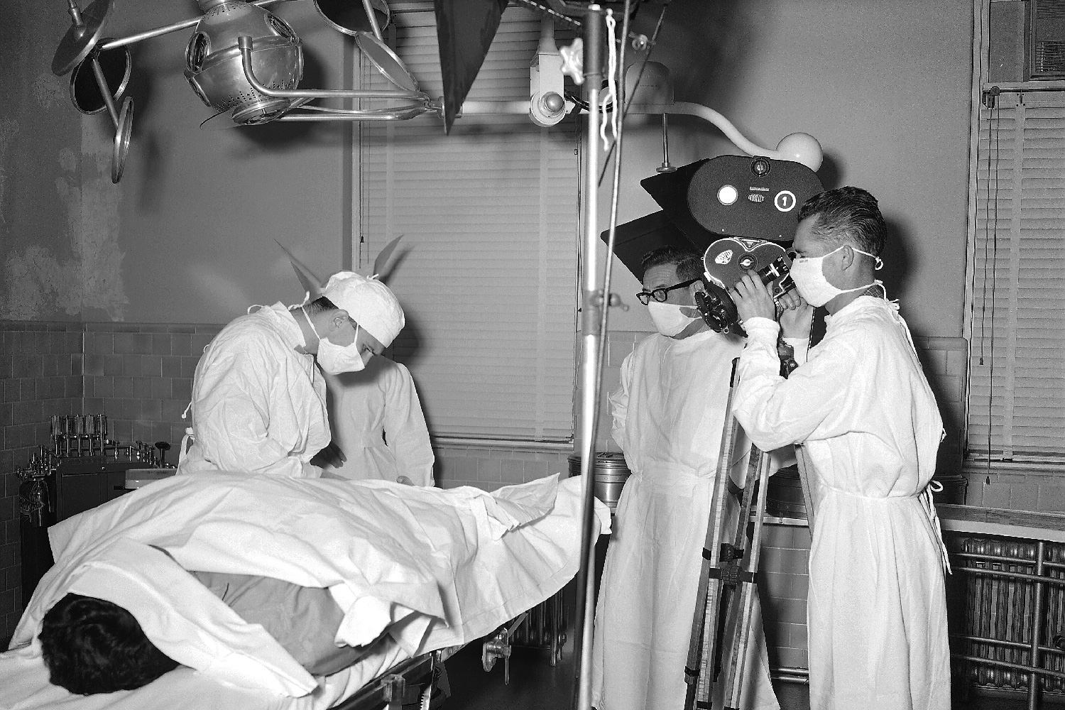 The photo shows an old fashioned operating room where all personnel, including the film crew, were dressed in gowns, and wore facemasks, in order to maintain a sterile environment.