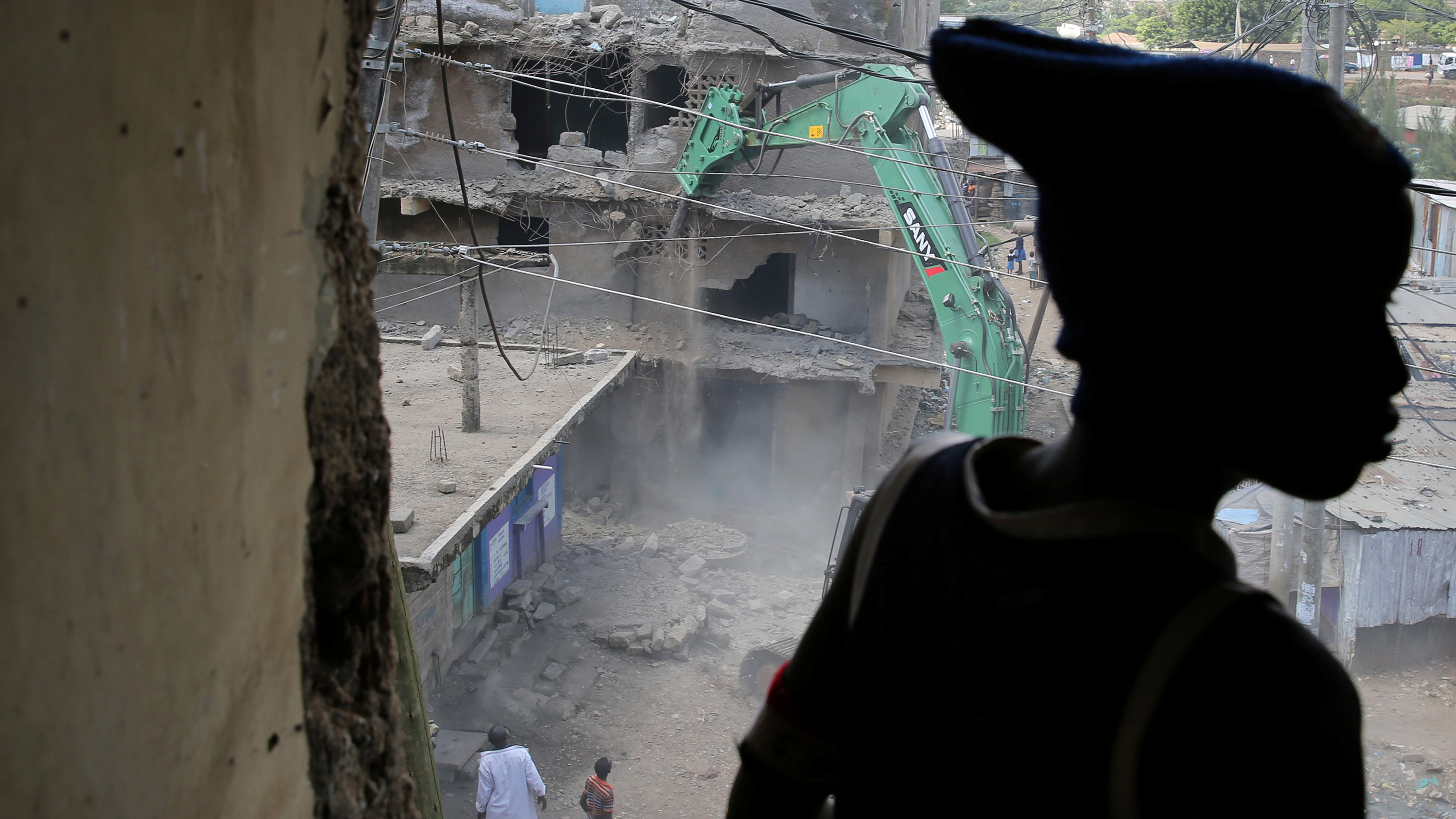 Image shows a building being torn down while the boy watches. He is silhouetted in the foreground.